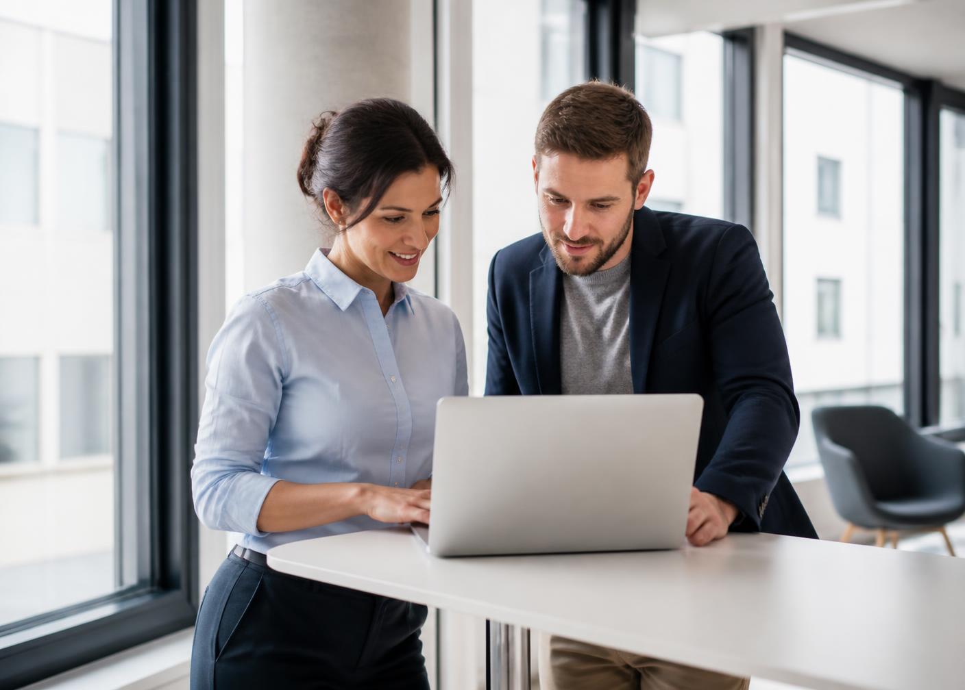 Two colleagues in smart casual attire collaborating around a laptop in a bright modern office